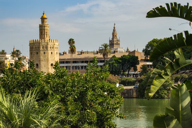 Севилья, Испания - SEPT. 23, 2013: Torre del Oro с Ла Giralda в расстоянии и реке на переднем плане стоковое изображение rf Севилья, Испания - SEPT. 23, 2013: Torre del Oro с Ла Giralda в расстоянии и реке на переднем плане стоковое изображение rf