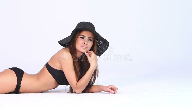 Сексуальная женщина в черных бикини и шляпе на белизне