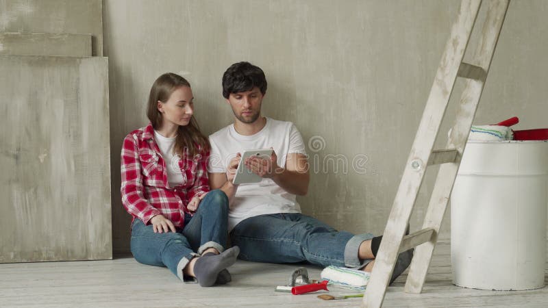 семейная пара использует цифровой планшет во время ремонта в новом доме. молодая пара сидит на полу с планшетом