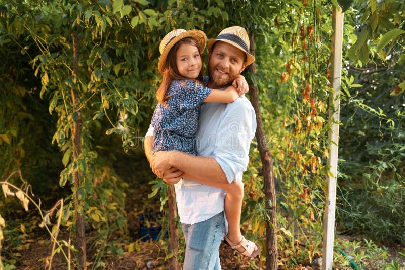 Семейный отпуск. счастливый бородатый отец в соломинке обнимает свою дочь. сад на заднем плане. концепция