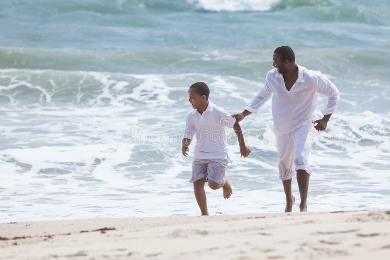 A happy African American family of father and son, men & boy child, running and having fun in the sand and waves of a sunny beach. A happy African American family of father and son, men & boy child, running and having fun in the sand and waves of a sunny beach