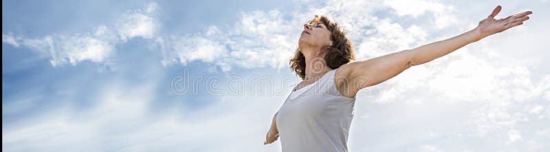 Female freedom - zen middle aged yoga woman opening up her chakra with arms raised,practicing meditation for freedom over summer blue sky,low angle view, long banner. Female freedom - zen middle aged yoga woman opening up her chakra with arms raised,practicing meditation for freedom over summer blue sky,low angle view, long banner