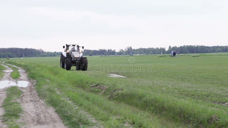 Серые езды трактора на зеленом поле