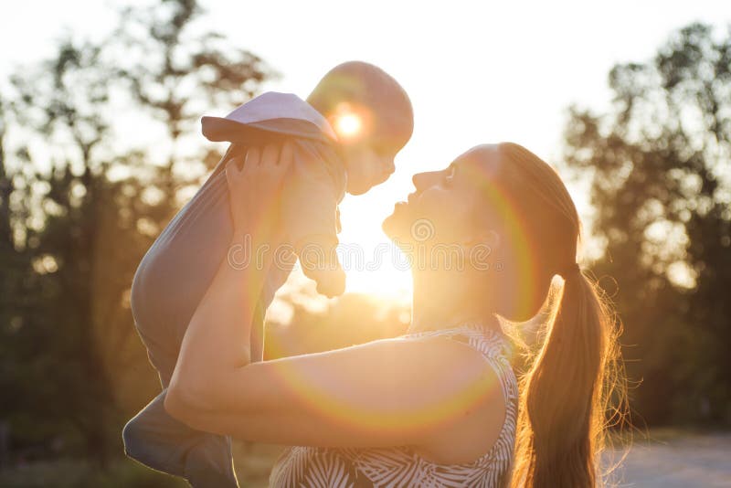 Backlight silhouette of a mother raising her kid son at sunset with the sun in the middle. Happy mom holding her cute baby on sunset background. Backlight silhouette of a mother raising her kid son at sunset with the sun in the middle. Happy mom holding her cute baby on sunset background.