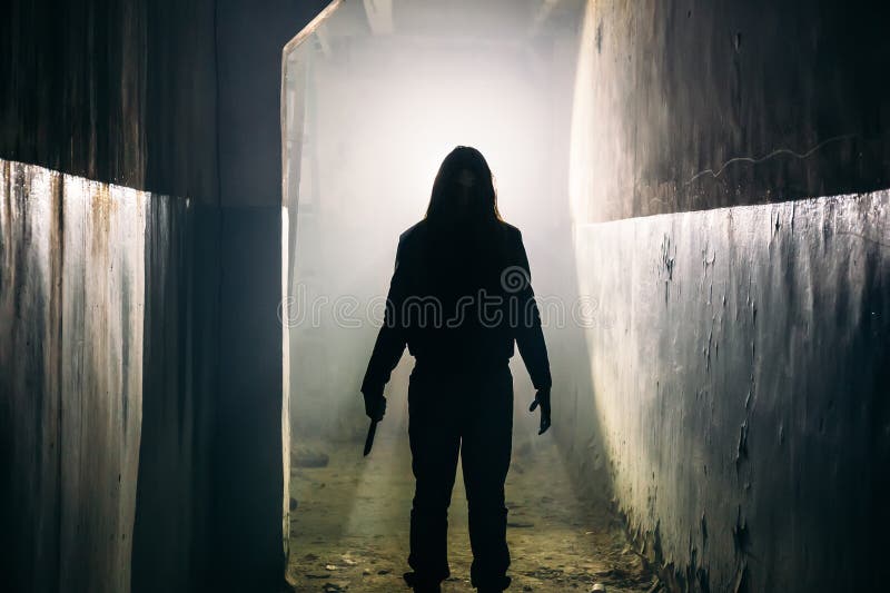 Silhouette of man maniac or killer or horror murderer with knife in hand in dark creepy and spooky corridor. Criminal robber or rapist concept in thriller atmosphere, toned. Silhouette of man maniac or killer or horror murderer with knife in hand in dark creepy and spooky corridor. Criminal robber or rapist concept in thriller atmosphere, toned