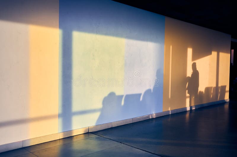 A silhouette of a man on a stone wall at the airport with space to copy. Shadows of people and chairs. Yellow and blue shades of light on the wall. High quality photo. A silhouette of a man on a stone wall at the airport with space to copy. Shadows of people and chairs. Yellow and blue shades of light on the wall. High quality photo