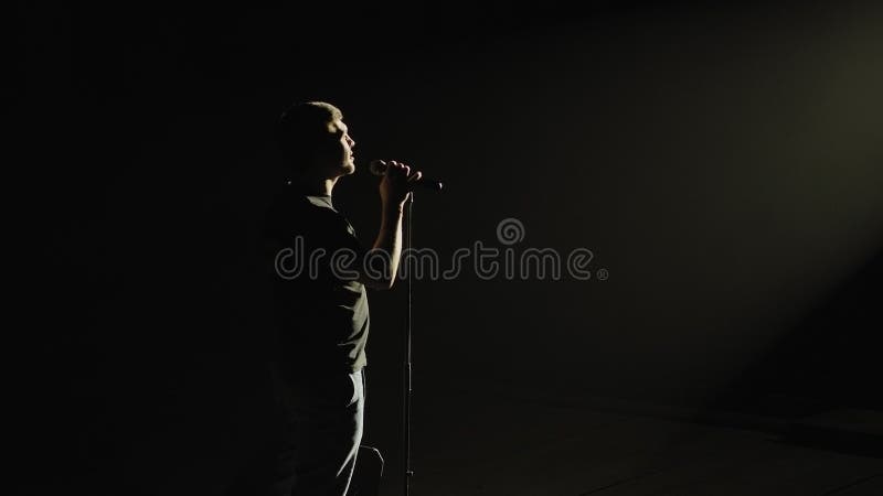 Силуэт человека на сцене в темноте с микрофоном.