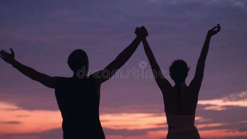 силуэтная пара поднимает руки на пляже океана празднуя счастливые моменты или победу вместе летом