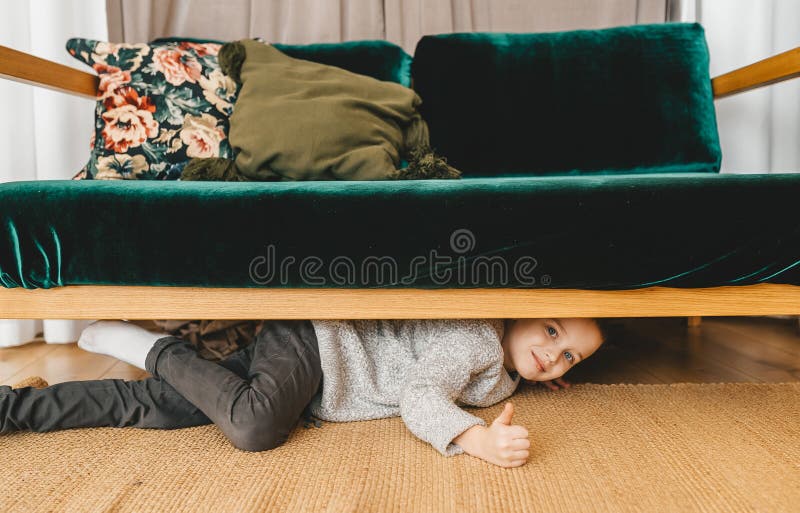 Симпатичный парень peeking из-под кровати. Мальчик, играя в прятки стоковая фотография