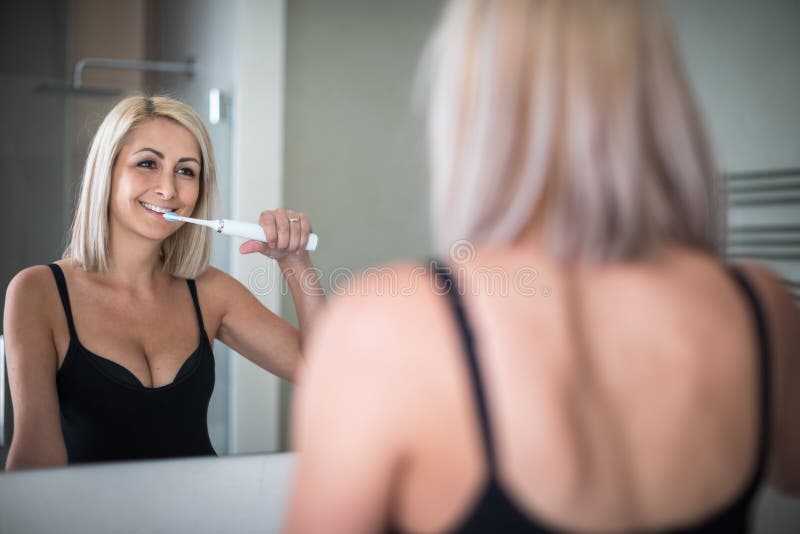 Pretty, middle aged woman brushing her teeth with braces in a modern design bathroom. Pretty, middle aged woman brushing her teeth with braces in a modern design bathroom