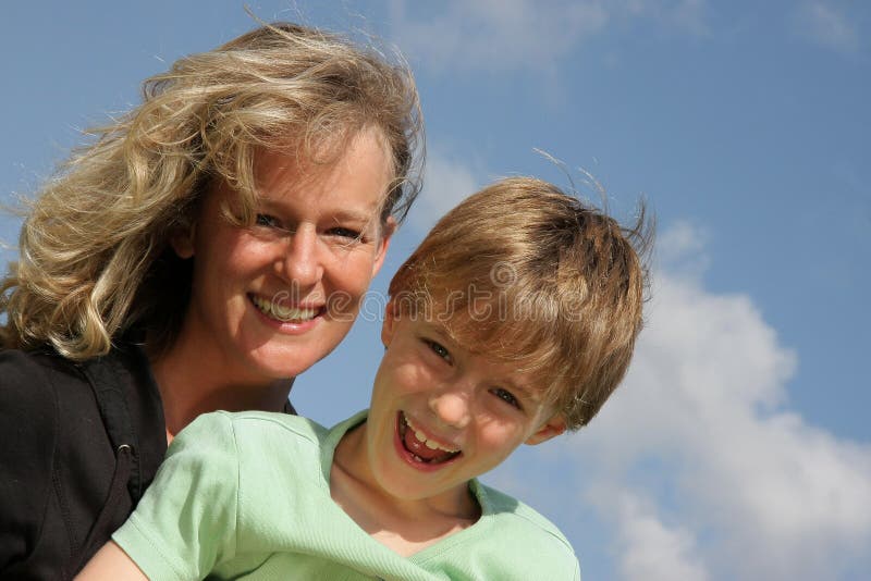 A beautiful smiling mother with her 7-years old laughing son photographed in the summer sun with blue sky and clouds in the background. A beautiful smiling mother with her 7-years old laughing son photographed in the summer sun with blue sky and clouds in the background