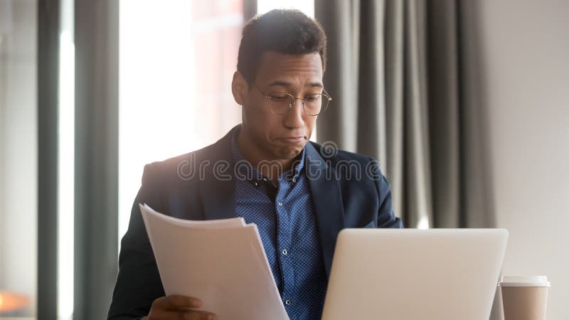 Смущенный черный мужской работник чувствует неуверенные читая документы обработки документов стоковая фотография Смущенный черный мужской работник чувствует неуверенные читая документы обработки документов стоковая фотография