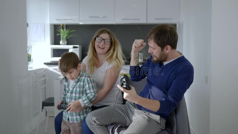 Современная семья, мама при сын и папа играя в видеоигре сидя на стуле