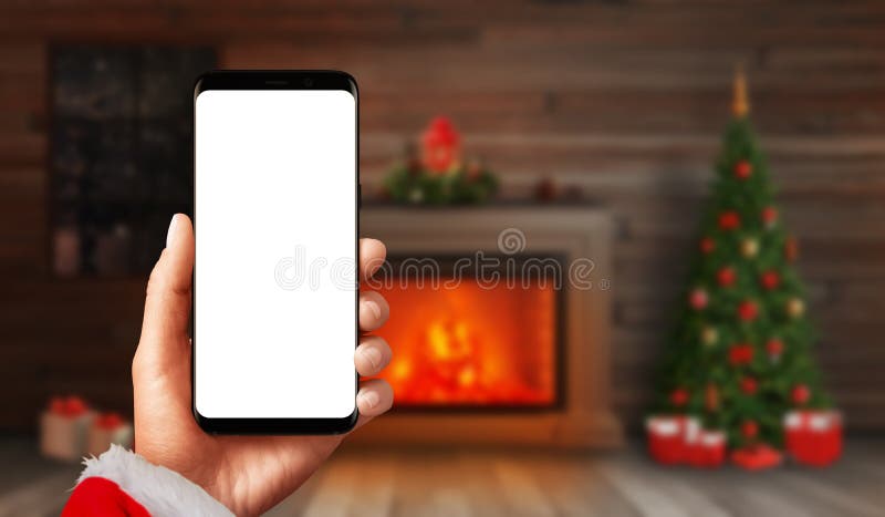 Современный макет смартфона в Санта-Клаусе с камином и рождественской елкой с декорациями и подарками на заднем плане стоковые фото