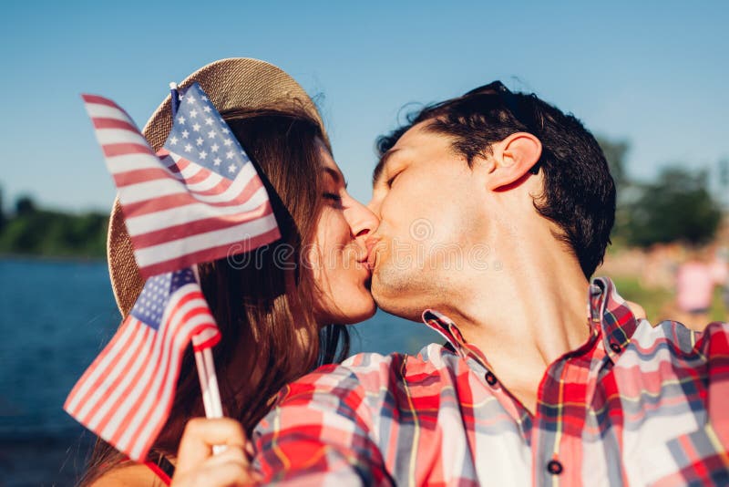 Соедините в любов целуя и держа флаг США Люди празднуя День независимости Америки стоковое изображение rf Соедините в любов целуя и держа флаг США Люди празднуя День независимости Америки стоковое изображение rf