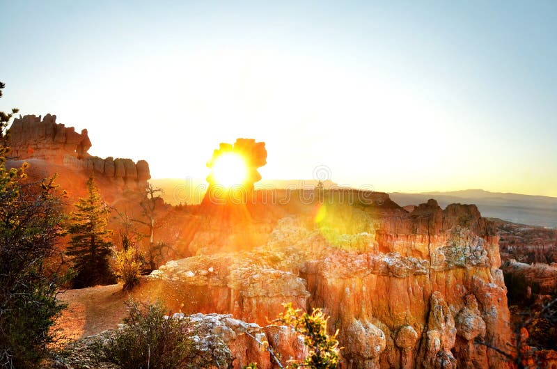 Солнце, сверкающее сквозь дыру в скале на рассвете в Брайсе Каньоне, с сенсфлер