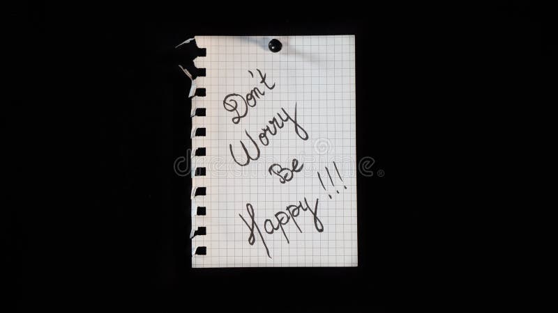 Hand written message on a ripped notebook sheet  "Don't worry be happy"  on black background. Hand written message on a ripped notebook sheet  "Don't worry be happy"  on black background