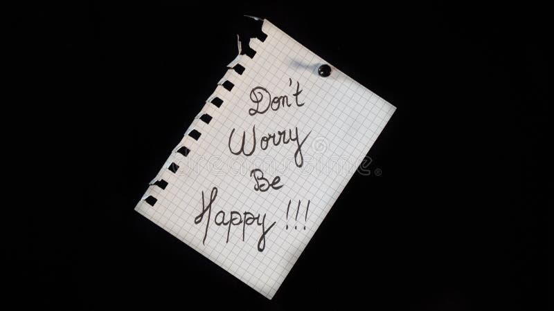 Hand written message on a ripped notebook sheet  "Don't worry be happy"  on black background. Hand written message on a ripped notebook sheet  "Don't worry be happy"  on black background