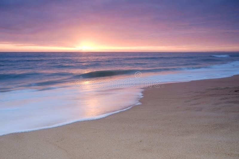 Спокойный пляж развевает во время захода солнца