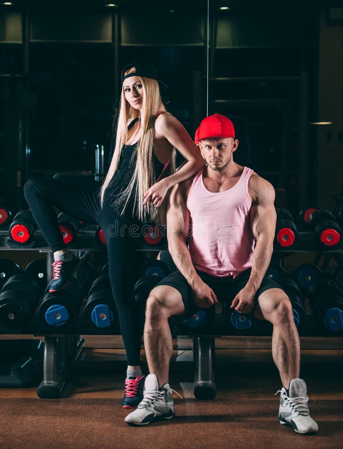 Спорт, культуризм, поднятие тяжестей, образ жизни и концепция людей - молодая красивая пара в стильных одеждах сидя a стоковое фото rf Спорт, культуризм, поднятие тяжестей, образ жизни и концепция людей - молодая красивая пара в стильных одеждах сидя a стоковое фото rf