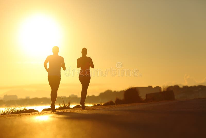 Silhouette of a couple practicing sport running at sunset on the road. Silhouette of a couple practicing sport running at sunset on the road