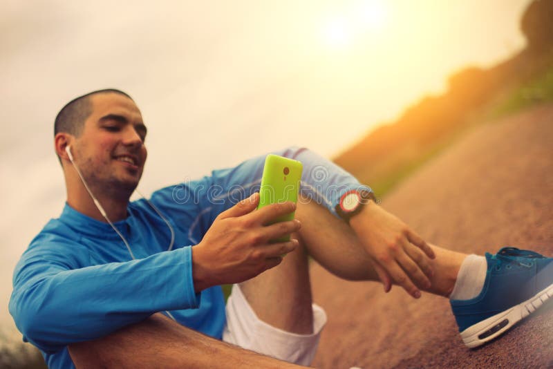 Спортсмен при часы и наушники смотря smartphone стоковые фотографии rf Спортсмен при часы и наушники смотря smartphone стоковые фотографии rf