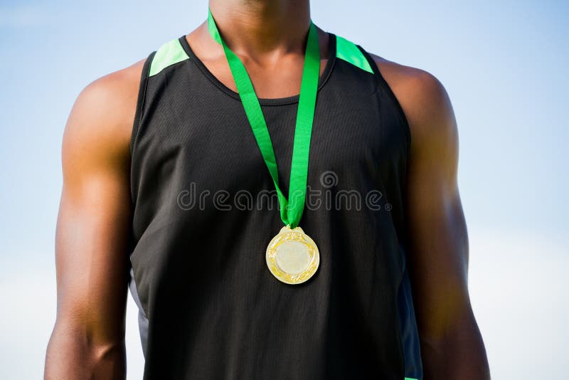 Mid section of athlete posing with gold medal around his neck on a sunny day. Mid section of athlete posing with gold medal around his neck on a sunny day