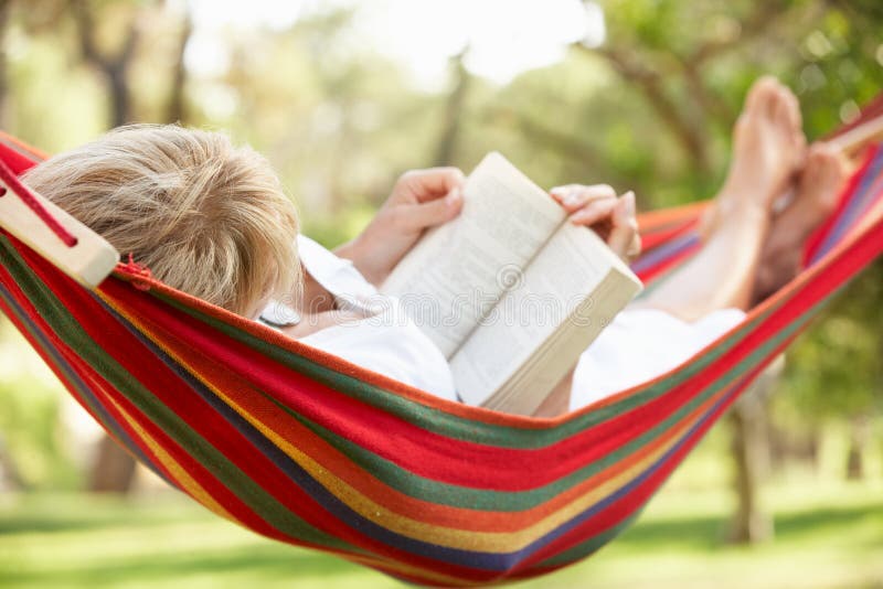 Старшая женщина ослабляя в гамаке с книгой стоковое изображение