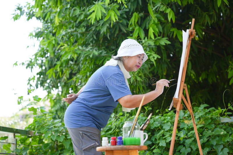 Старшая женщина рисует на свежем воздухе на Easel Mature Artist Создание искусства в природе пожилая леди наслаждаясь наружной жив стоковые изображения