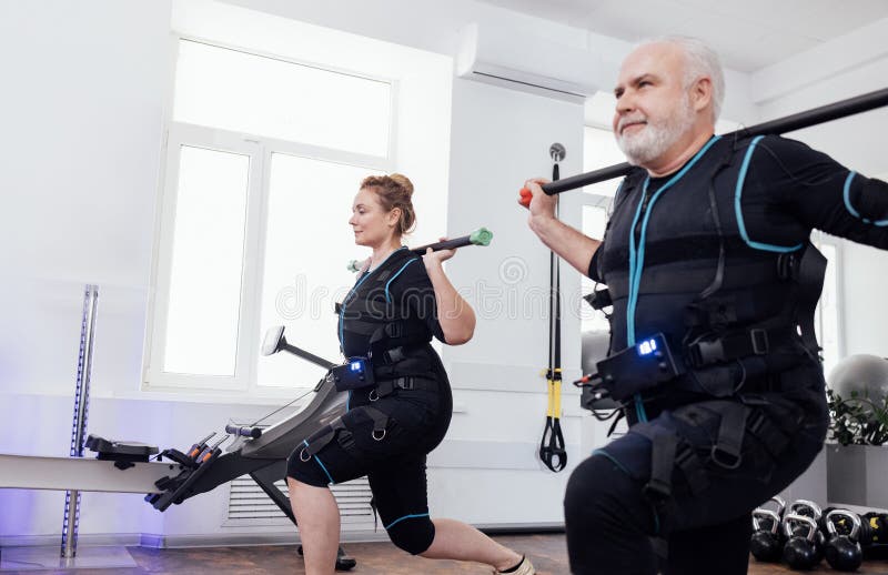 старшая спортивная пара в костюмах ems делает электрическую стимуляцию мышц тренировки с гимнастическими палками стоковые фотографии rf