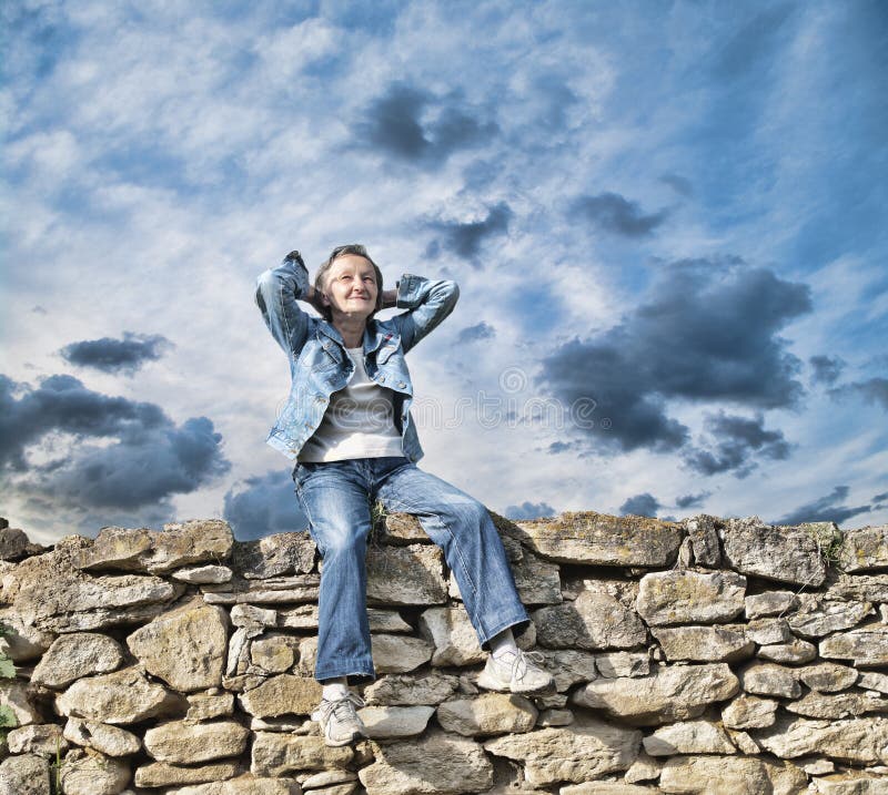 Happy senior adult woman smiling relaxed sitting on old wall. Happy senior adult woman smiling relaxed sitting on old wall.