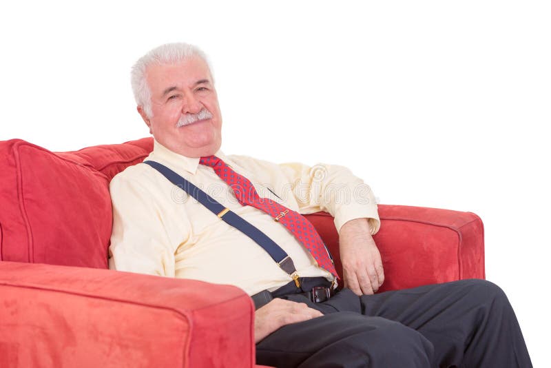 Senior grey-haired gentleman with a moustache wearing braces relaxing in a comfortable red armchair on a white background. Senior grey-haired gentleman with a moustache wearing braces relaxing in a comfortable red armchair on a white background