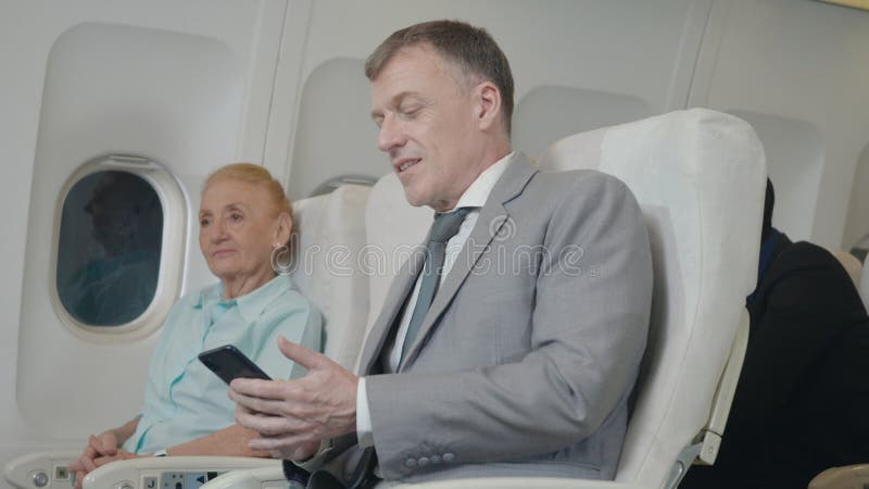 старший пассажир, использующий смартфон в самолете, путешествует для безопасного полета стоковые изображения