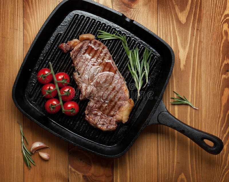 Sirloin steak with rosemary and cherry tomatoes on frying pan over wooden table. Sirloin steak with rosemary and cherry tomatoes on frying pan over wooden table