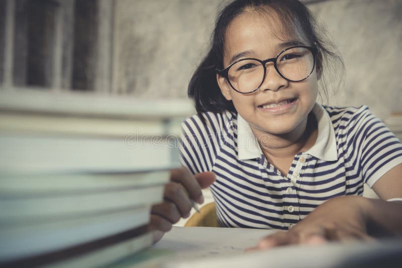 Asian teenager wearing eye glasses doing home work with stack of school book foreground. Asian teenager wearing eye glasses doing home work with stack of school book foreground