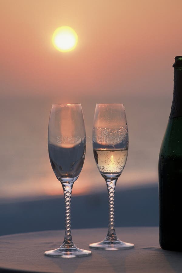 2 glasses 1 full of champagne and bottle at sunset. 2 glasses 1 full of champagne and bottle at sunset