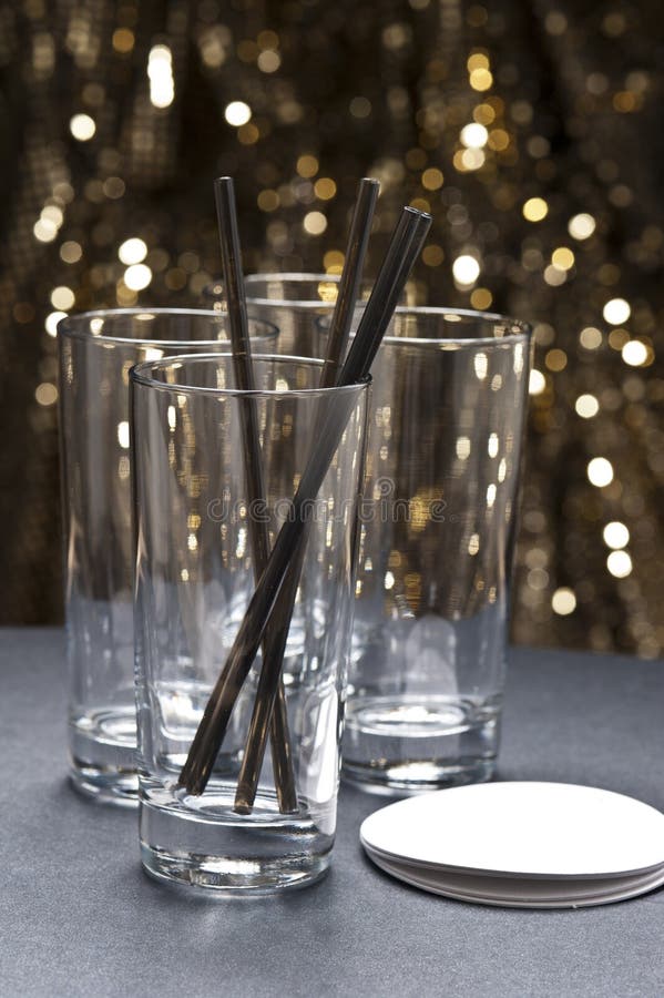 Long drink glasses with straws and coaster in front of glitter background in front of gold glitter background. Long drink glasses with straws and coaster in front of glitter background in front of gold glitter background