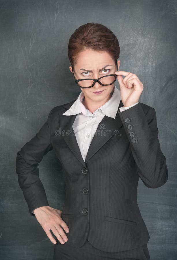 Strict teacher looking at someone on the school blackboard background. Strict teacher looking at someone on the school blackboard background