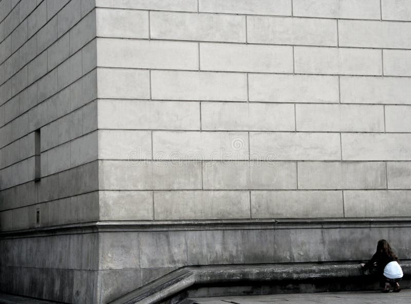 Corner of gray concrete building with blocks overlapping in brick style, woman kneeling in foreground. Corner of gray concrete building with blocks overlapping in brick style, woman kneeling in foreground.