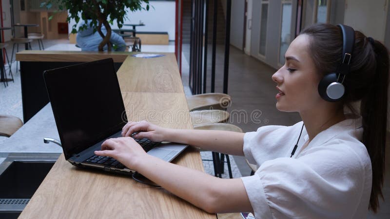 Студентка использует портативный компьютер и интернет для обучения. Молодая женщина в наушниках стоковая фотография