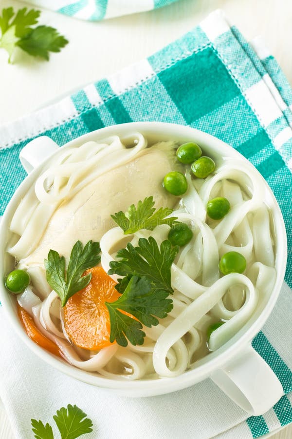 Chicken and rice noodle soup with peas topped with parsley leaves in white bowl. Chicken and rice noodle soup with peas topped with parsley leaves in white bowl