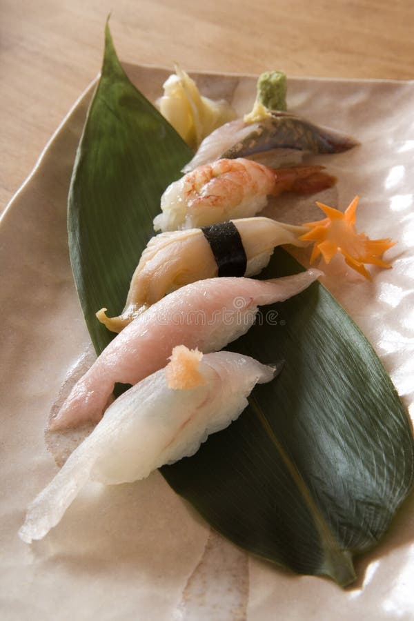 Photographs of sushi on a banana leaf on a square plate on a wood table. Photographs of sushi on a banana leaf on a square plate on a wood table