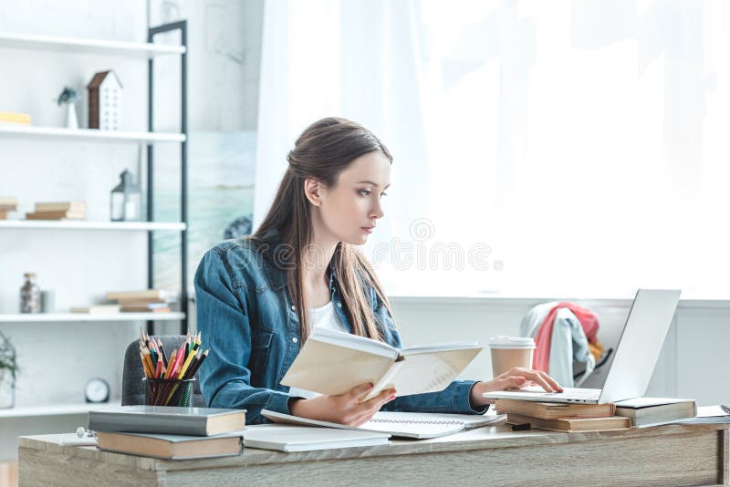 сфокусированные книга удерживания девочка-подростка и ноутбук использования пока изучающ стоковые фото сфокусированные книга удерживания девочка-подростка и ноутбук использования пока изучающ стоковые фото