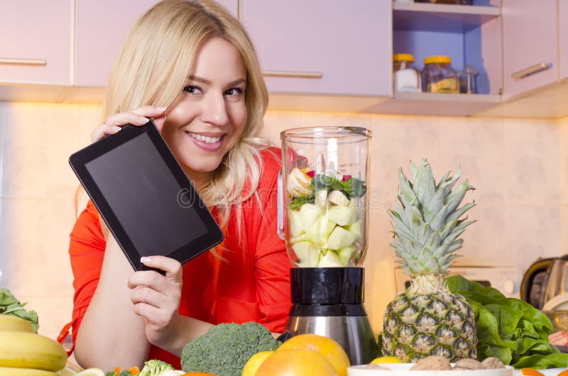 Счастливая женщина держа таблетку рядом с juicer полный плодоовощ стоковое изображение Счастливая женщина держа таблетку рядом с juicer полный плодоовощ стоковое изображение