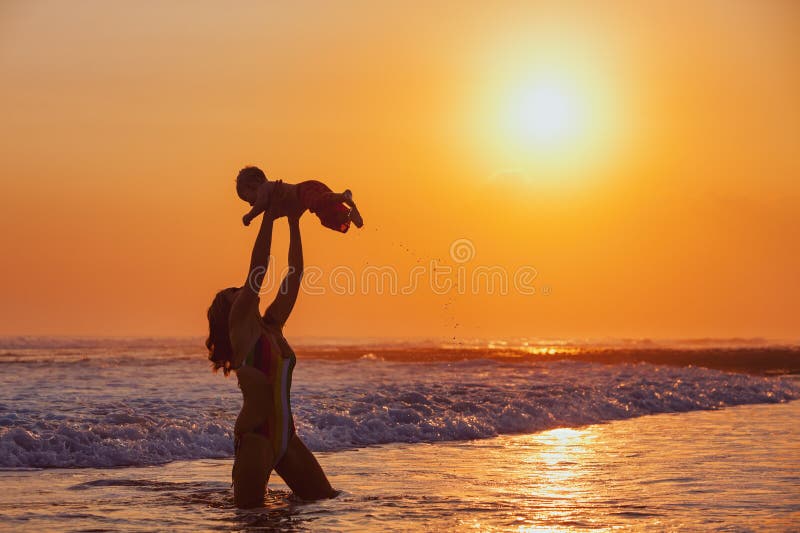 Happy family swimming fun on sea beach - mother tossing up baby son into mid air, catching on sunset sky, sun background Parents outdoor activity, child lifestyle on summer vacation in tropical island. Happy family swimming fun on sea beach - mother tossing up baby son into mid air, catching on sunset sky, sun background Parents outdoor activity, child lifestyle on summer vacation in tropical island
