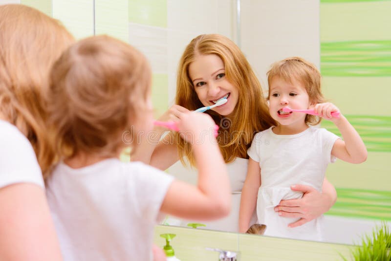 Happy family mother and daughter child girl brushing her teeth toothbrushes front of the mirror in the bathroom. Happy family mother and daughter child girl brushing her teeth toothbrushes front of the mirror in the bathroom
