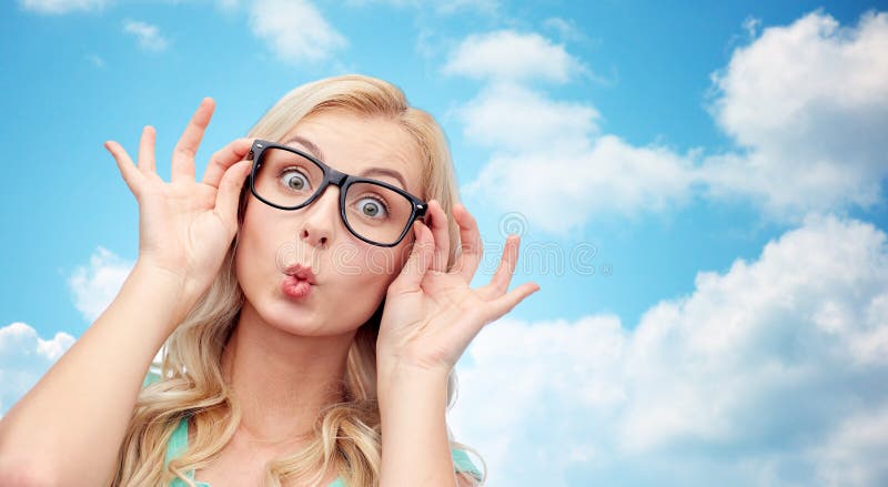 Vision, education and people concept - happy young woman or teenage girl glasses making funny fish face over blue sky and clouds background. Vision, education and people concept - happy young woman or teenage girl glasses making funny fish face over blue sky and clouds background