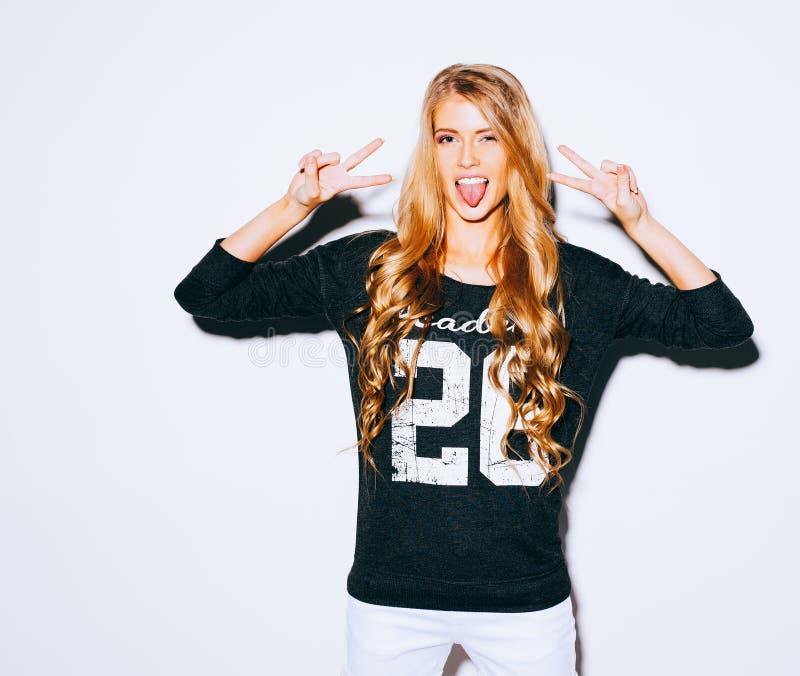 Happy Young Woman Showing Victory Sign and showing tongue On White Background. Indoor. Warm color. Hipster. Happy Young Woman Showing Victory Sign and showing tongue On White Background. Indoor. Warm color. Hipster.