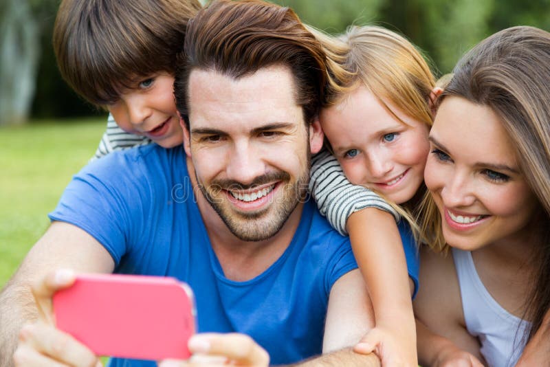 Счастливая молодая семья принимая selfies с ее smartphone в равенстве стоковое изображение Счастливая молодая семья принимая selfies с ее smartphone в равенстве стоковое изображение