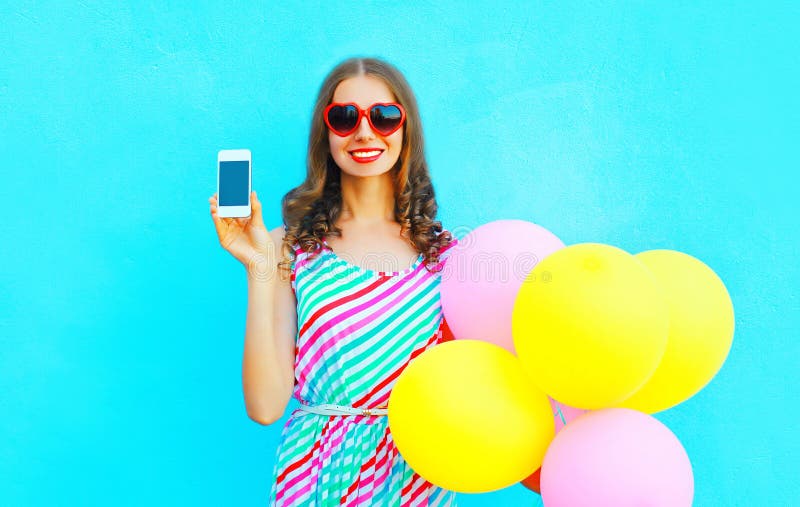 Счастливая усмехаясь женщина показывает smartphone держа воздух красочные воздушные шары стоковые изображения Счастливая усмехаясь женщина показывает smartphone держа воздух красочные воздушные шары стоковые изображения